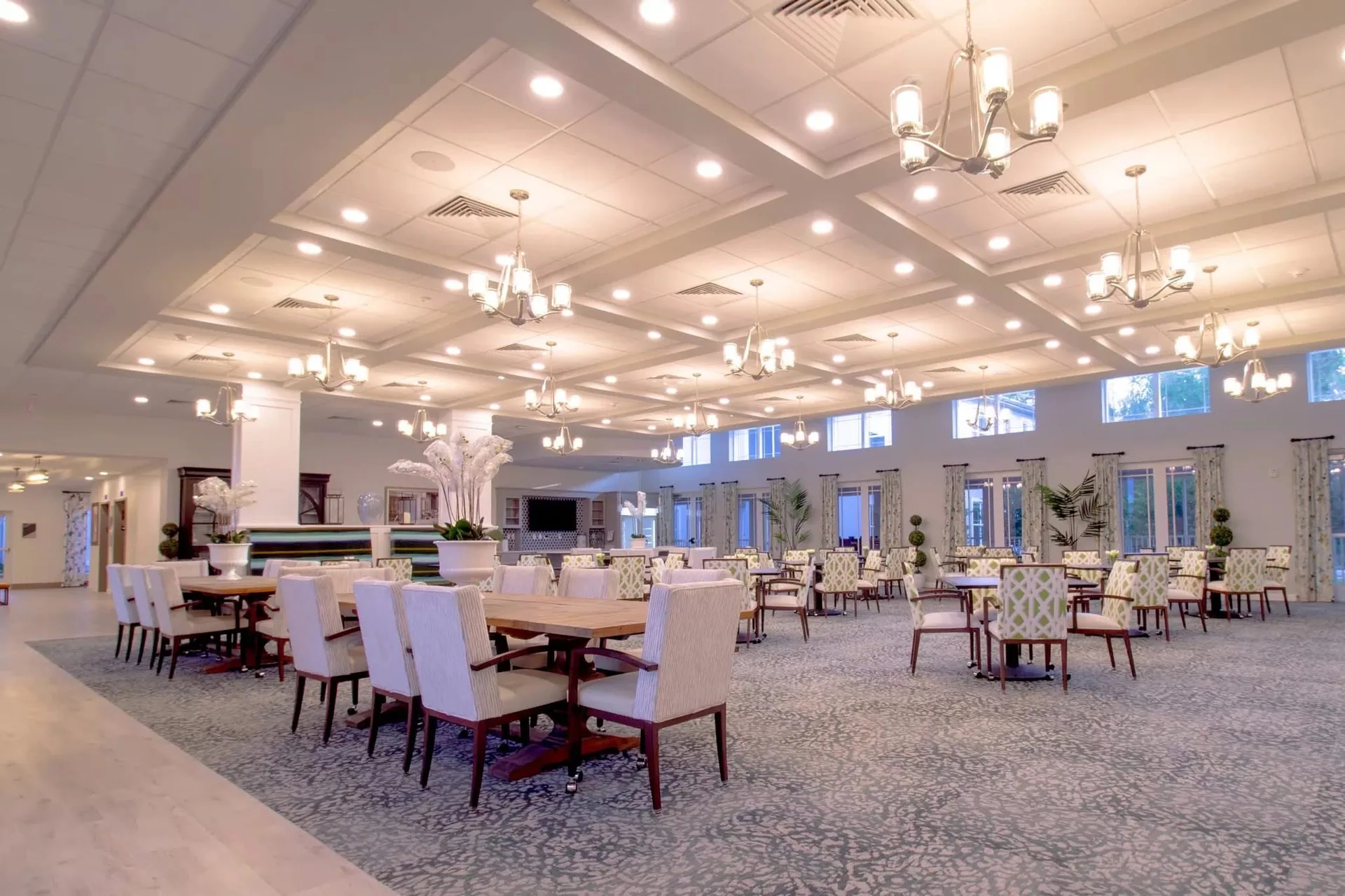 Large dining room with a coffered ceiling, chandeliers and tables arranged across the floor.